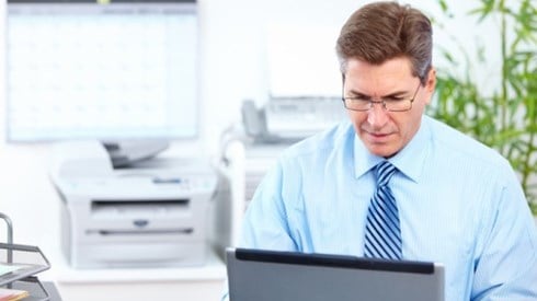 Businessman using laptop computer with office equipment blurred in the background