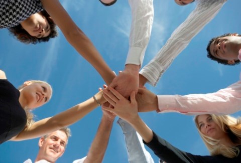 A group of people in a circle extending one arm and placing their hands on top of each in the middle