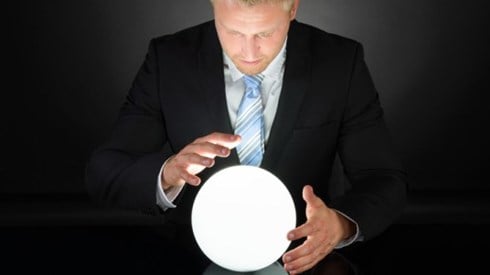 Man in black suit looking at glowing crystal ball with his hands surrounding it