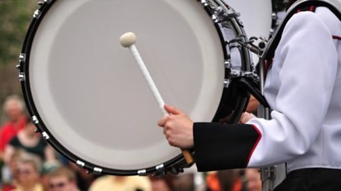 Drummer wearing black and white band uniform beating large bass drum in parade