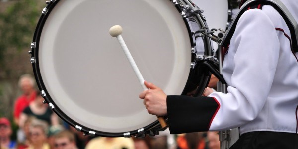 Drummer wearing black and white band uniform beating large bass drum in parade