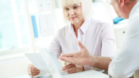 Mature businesswoman looking at document while man speaks to her
