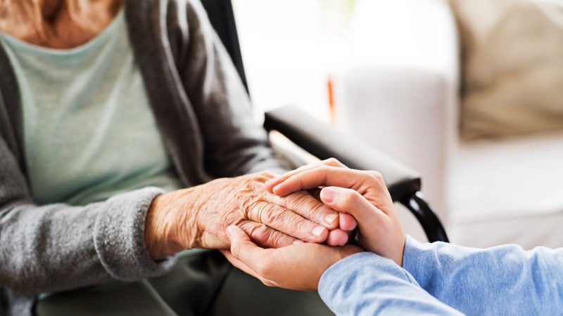 An elderly woman sitting in a chair with her hand held gently by two hands