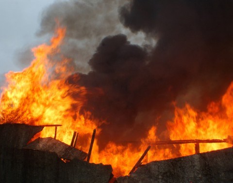 A building is being consumed by large flames of fire and black smoke.