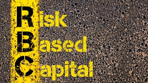 Acronym RBC in black letters on yellow paint stripe with risk-based capital written in yellow on black asphalt background